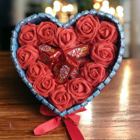 Kit Kat minis op een hart omringt met roden rozen. Het hele hart is omringt met chocolaatjes met cremevulling