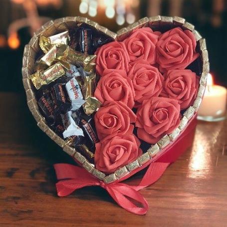 Toblerone mix op de helft van een hart, op de andere helft van het hart rode foam rozen. Hart is omringt met Merci chocolaatj