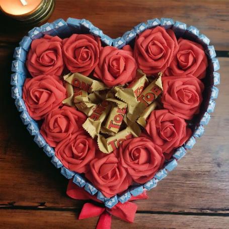 Toblerone amandel op een hart omringt met rode foam rozen. Hart zelf omringt met chocolaatjes met cremevulling