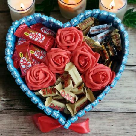 Toblerone mix, amandel en kit kat op een hart met 6 rozen. Hart is omringt met chocolaatjes met cremevulling.