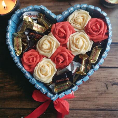 Toblerone mix op een hart met in het midden een strook van witte en rode rozen. Aan de zijkanten is het hart omringt met choc